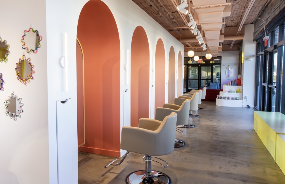 A long corridor with multiple chairs and embedded mirrors in front of them with a large window for light.