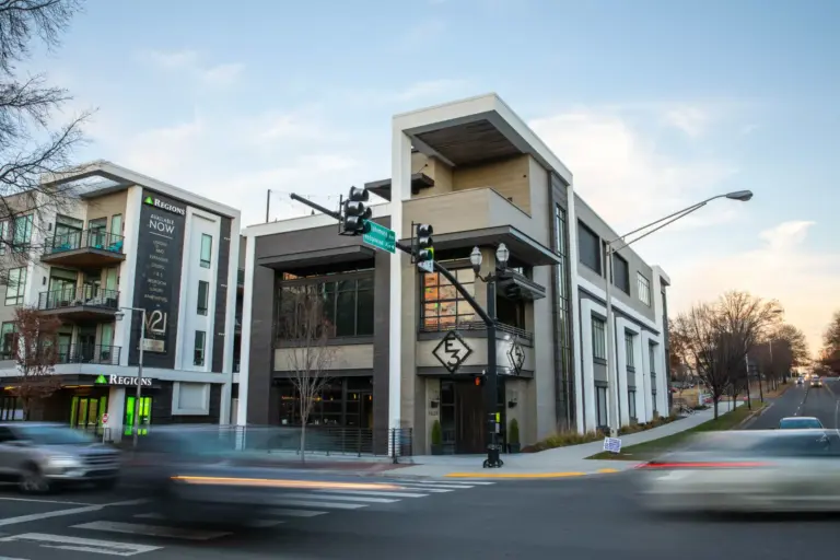 Exterior of a modern white and mud grey corner building, which has windows, and an E3 metal logo on it with planters around its entrance.