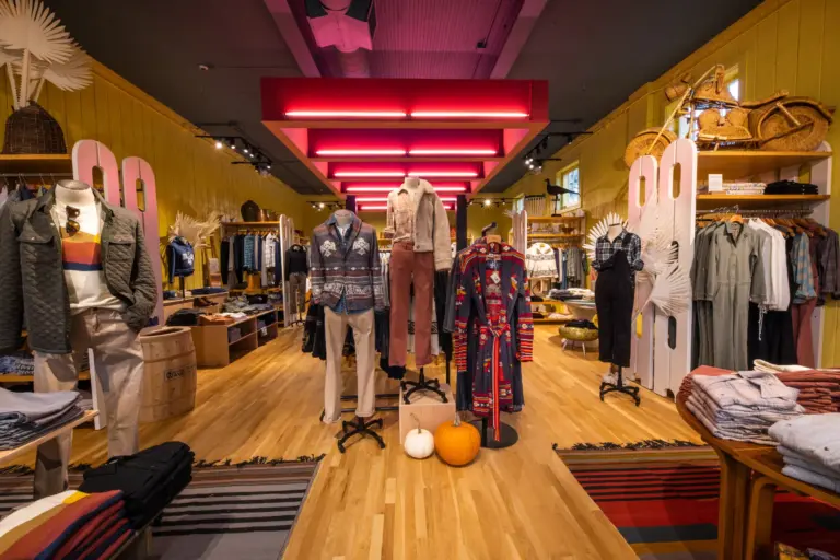 A Native American-themed clothing shop with red lights on roof, white feather fans, rugs for decor, baggy women's clothing and men's jackets.