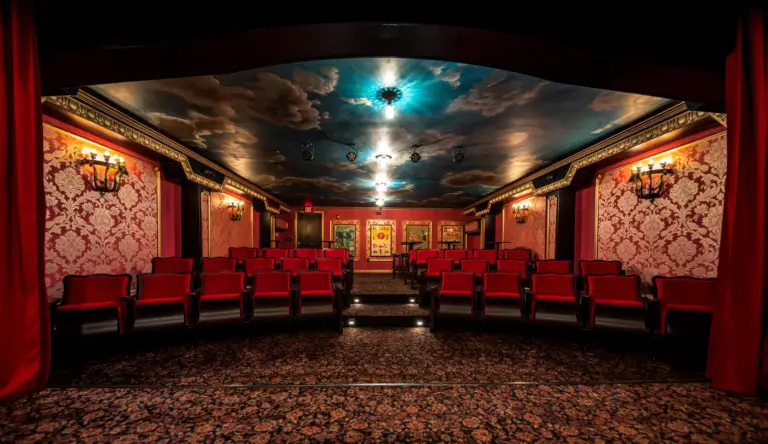 A theater room with a royal theme, chairs lined at both sides in rows, roof having sky look, and antique lights on the wall.