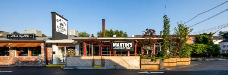 Exterior view of the building with red pillars and white doors and a banner saying "Martin Bar-B-Que Joint" and " Whole Hog BBQ".