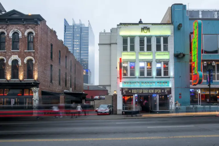 White building with glass windows, doors, NUDIE's HONKY TONK in white neonlights, TOP ROOF BAR OPEN NOW on a banner at the front.