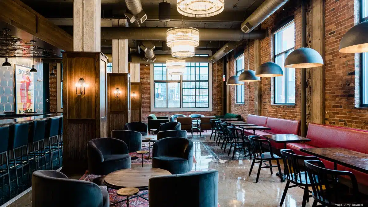 Antique-themed sitting area with maroon sofas, brick walls, wooden cupboards, black hanging lights, candles, and marble floors.