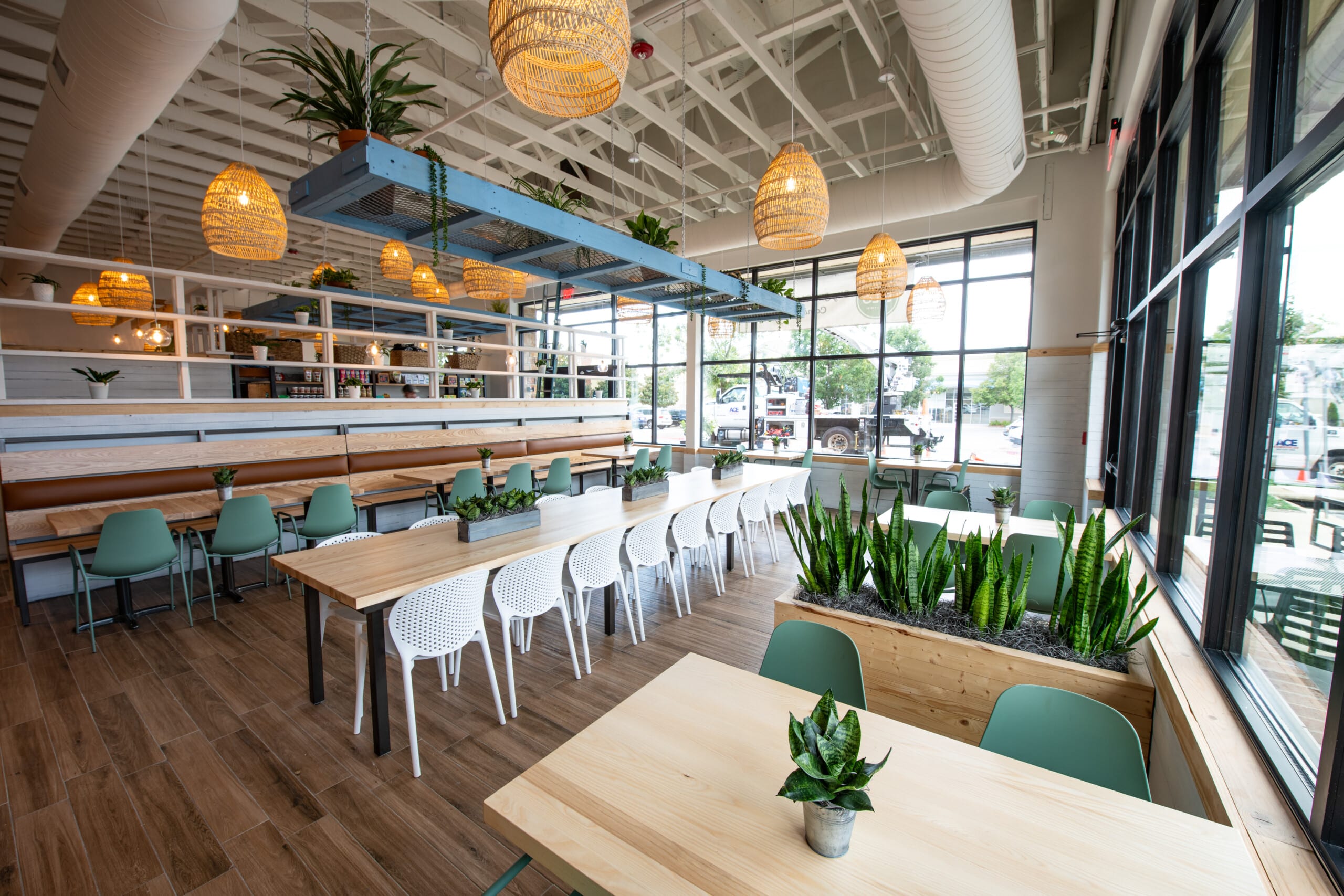 A nature themed seating area with wooden benches and tables, planters with snake plants, hanging lights, and sage green and white chairs.